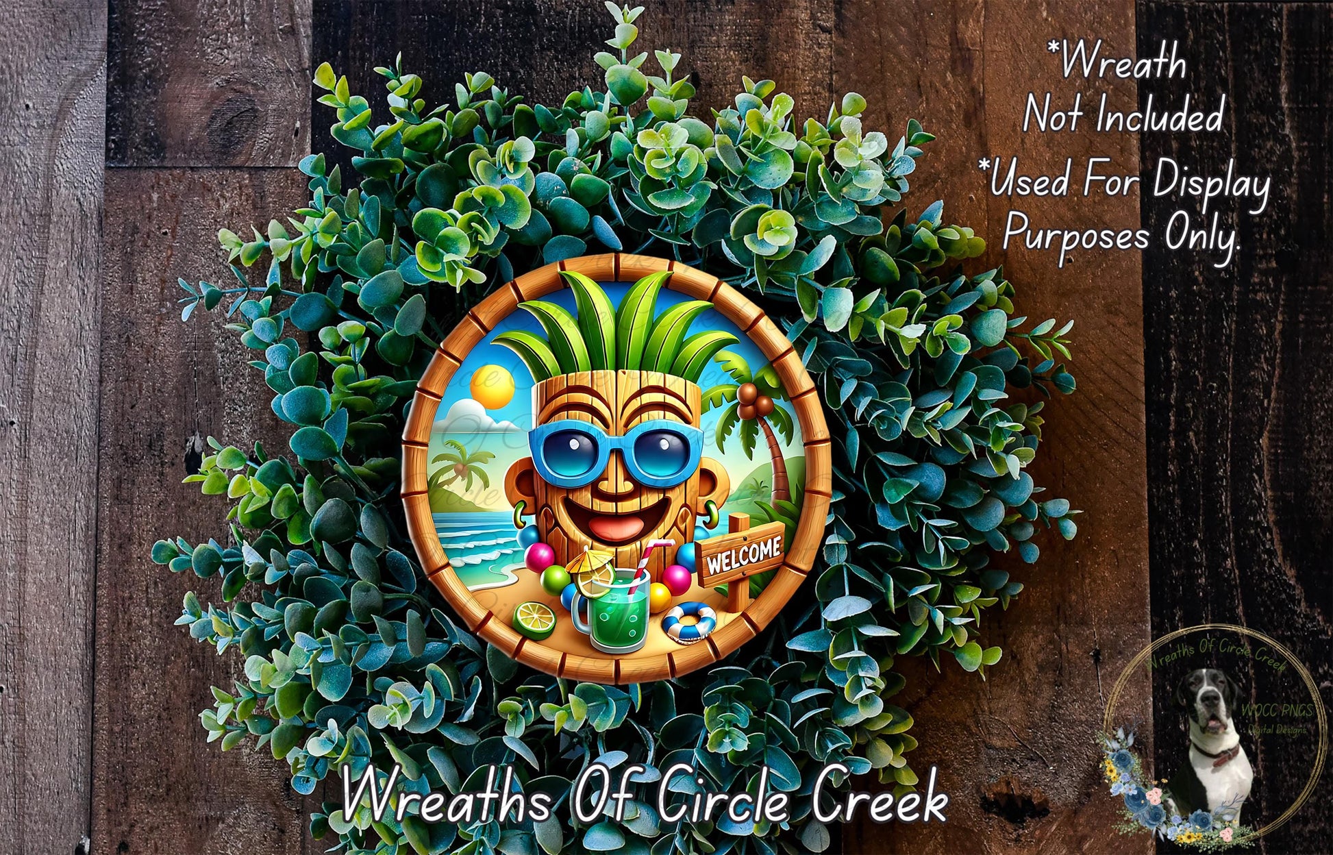 A wreath with a tropical theme, featuring a tiki mask, sunglasses, and a welcome sign. The wreath is surrounded by greenery and placed on a wooden surface.
