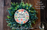 A wreath made of various green plants and colorful paw prints, with a circular sign that says &quot;All Paws Welcome&quot; in the center.