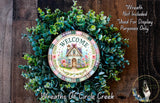 a wreath with a house design, surrounded by greenery, and a plate with a welcome message.