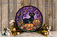 A Halloween-themed wreath featuring a black cat, two jack-o'-lanterns, and a purple background with a tree and flowers. The wreath is displayed on a wooden surface, surrounded by flowers and greenery.
