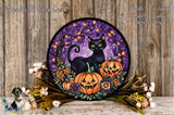 A Halloween-themed wreath featuring a black cat, two jack-o'-lanterns, and a purple background with a tree and flowers. The wreath is displayed on a wooden surface, surrounded by flowers and greenery.