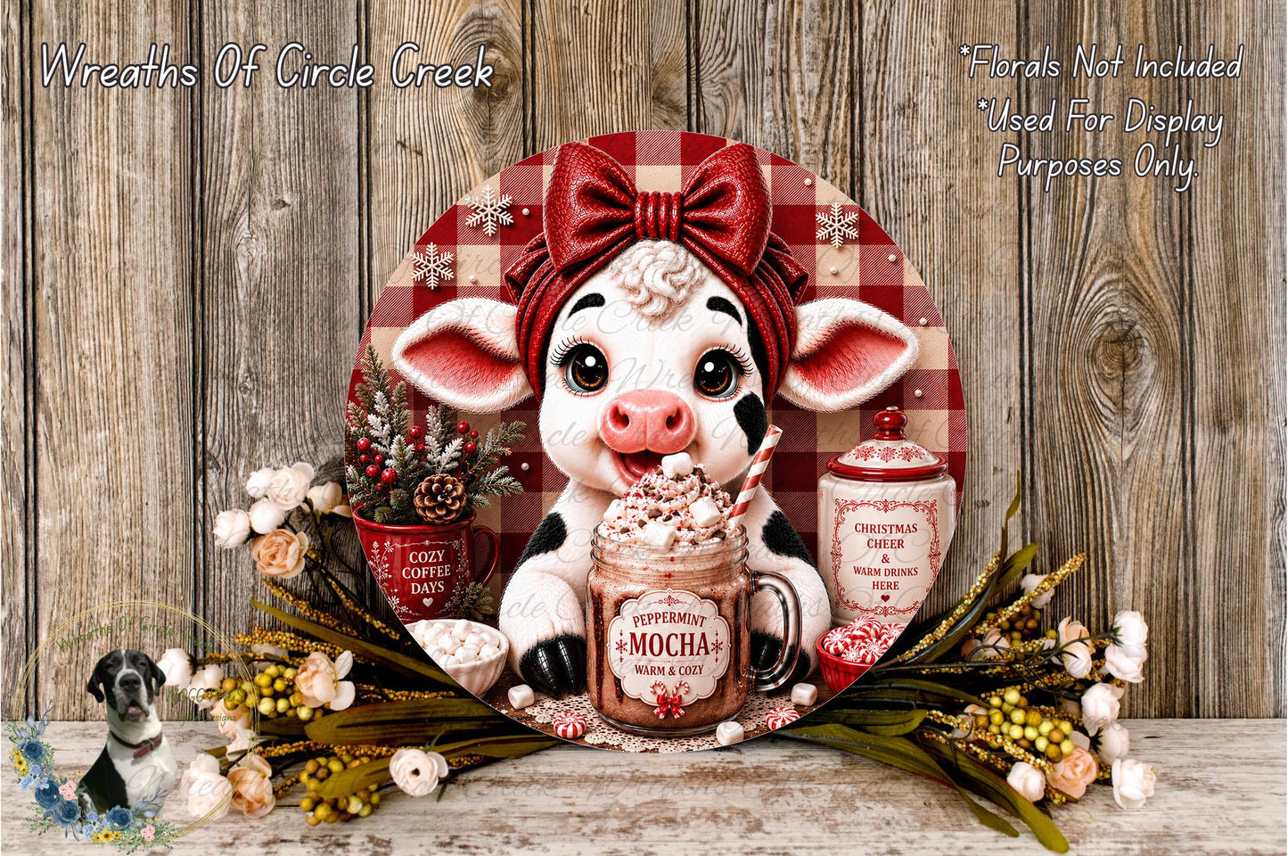 A decorative wreath featuring a cow wearing a red bow, surrounded by holiday-themed items such as a mug of peppermint mocha, a Christmas tree, and a pine cone.