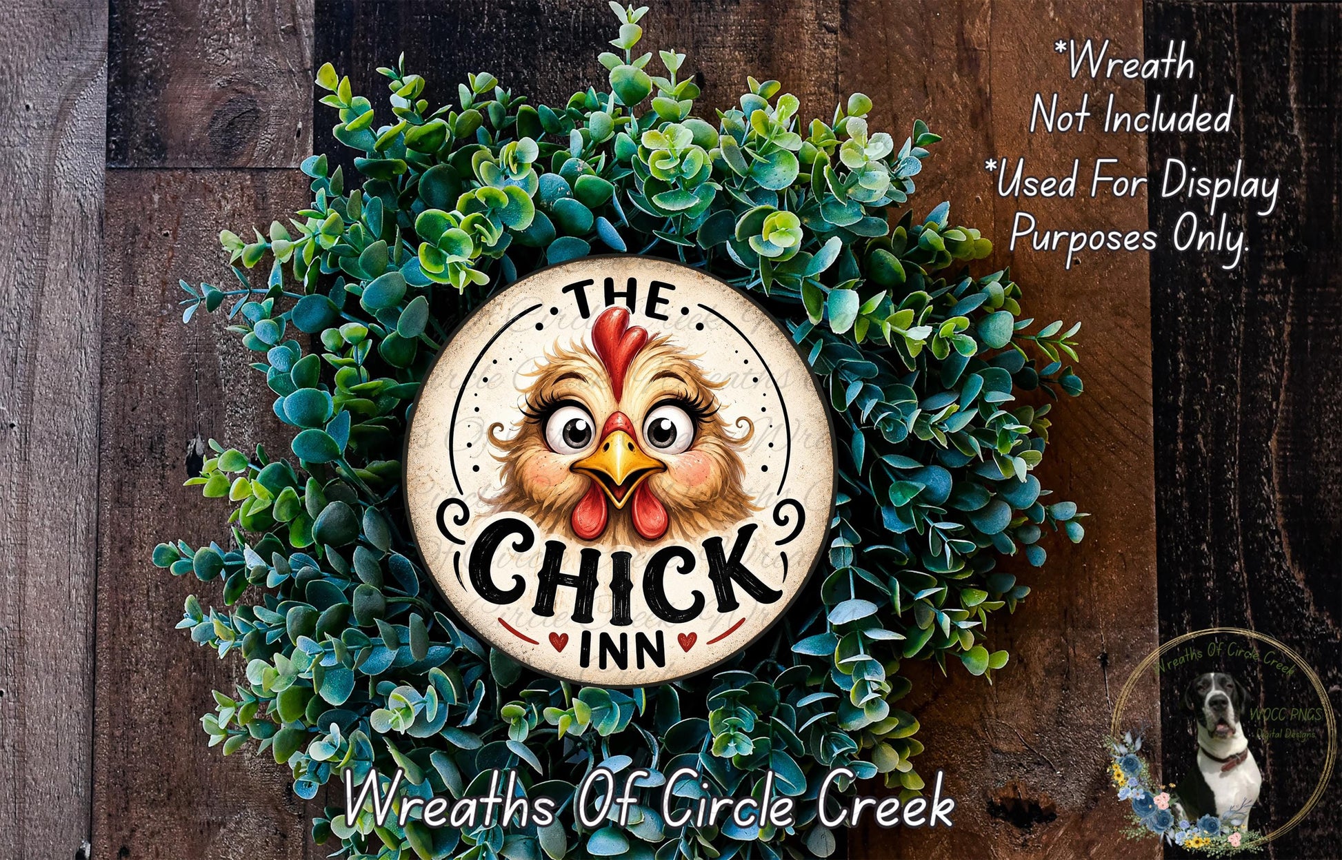 a wreath with a large, whimsical chicken face design at the center, surrounded by green foliage. The wreath is displayed on a wooden surface, and there is a small dog visible in the bottom right corner of the image.