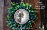 A wreath made of green leaves and a silver deer head, with a red ribbon around the deer's neck.
