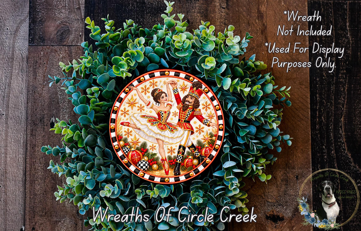 A decorative wreath made of green foliage and featuring a painted image of two dancers in a ballerina pose.