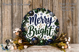 A festive wreath with the text "Merry & Bright" displayed on it, surrounded by various holiday decorations such as ornaments, flowers, and pine branches. The wreath is placed on a wooden surface, and there is a small dog in the background.