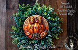 a wreath made of various greenery and a decorative orange pumpkin with a leopard print bow, placed on a wooden surface.
