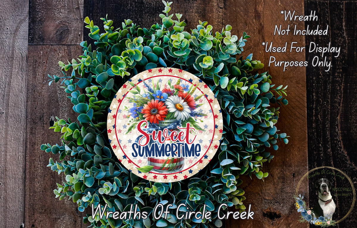 a wreath made of green leaves and flowers, with a patriotic-themed design. The wreath is displayed on a wooden surface, and there is a small dog in the bottom right corner of the image.