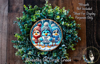 A wreath made of green leaves and flowers, featuring three cartoon birds wearing winter hats and holding signs. The wreath is displayed on a wooden surface, and there is a text overlay that reads "Wreath Not Included * Used For Display Purposes Only".