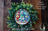A wreath made of green leaves and flowers, featuring three cartoon birds wearing winter hats and holding signs. The wreath is displayed on a wooden surface, and there is a text overlay that reads "Wreath Not Included * Used For Display Purposes Only".