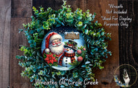 A wreath featuring a Santa Claus and a snowman, surrounded by greenery, with a "Merry Christmas" message. The wreath is displayed on a wooden surface, and there is a text overlay that states "Wreath Not Included * Used For Display Purposes Only".
