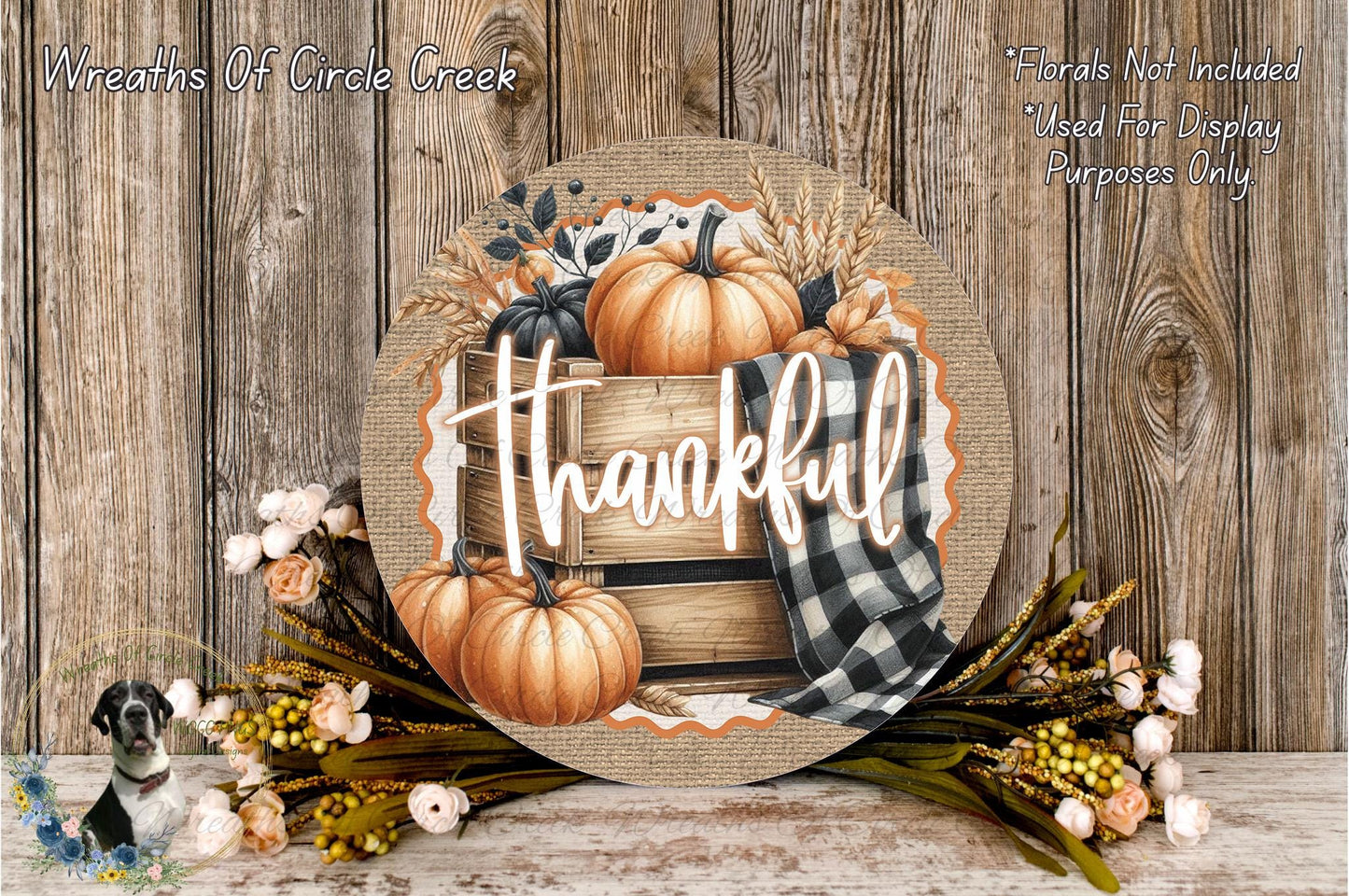 a round wooden sign with the word "Thankful" written on it, surrounded by autumn-themed decorations such as pumpkins, flowers, and a plaid cloth.