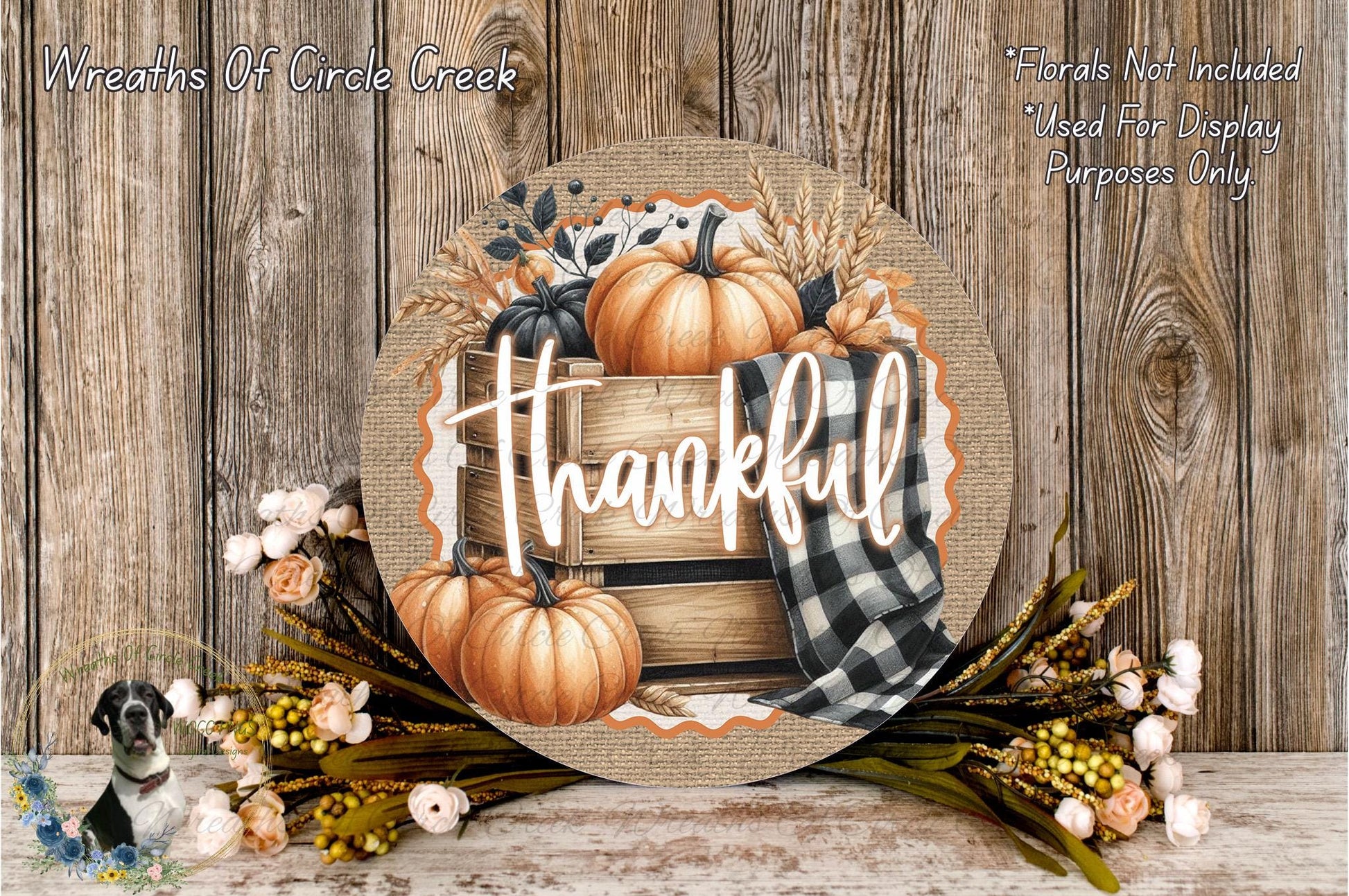 a round wooden sign with the word "Thankful" written on it, surrounded by autumn-themed decorations such as pumpkins, flowers, and a plaid cloth.