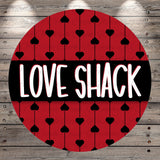 a circular design with a red background and a repeating pattern of black hearts. The phrase "LOVE SHACK" is prominently displayed in the center of the circle.
