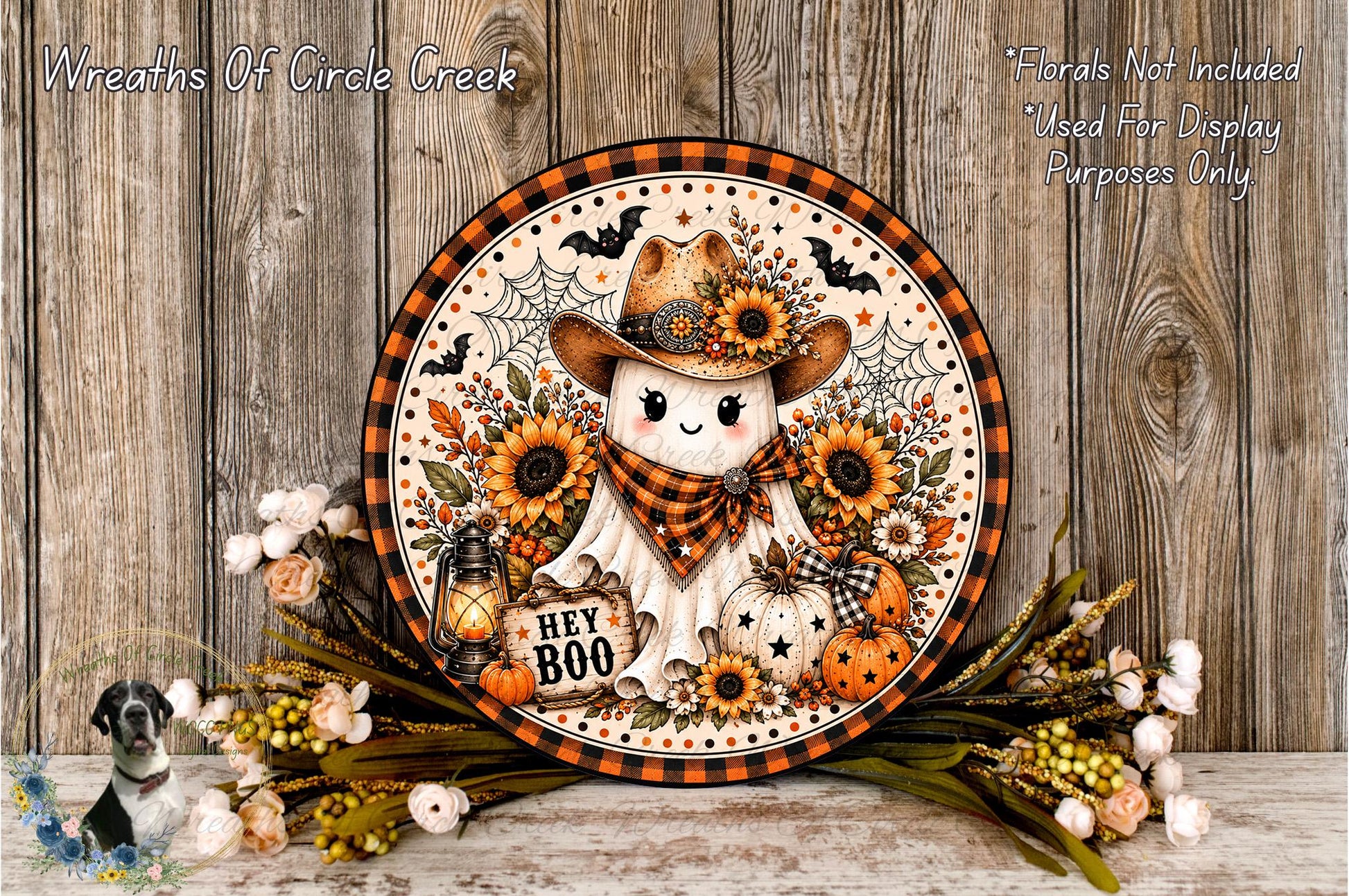 A decorative plate featuring a ghost wearing a cowboy hat and scarf, surrounded by autumn-themed elements such as sunflowers, pumpkins, and a lantern. The plate is placed on a wooden surface, with a wreath of flowers and a lantern nearby.