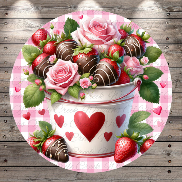 A bucket filled with chocolate-covered strawberries and roses, surrounded by hearts and leaves, set against a pink and white checkered background.