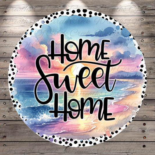A circular design with a watercolor-style background depicting a sunset over a beach. The text "Home Sweet Home" is written in a cursive font in the center of the design.