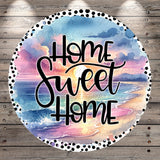A circular design with a watercolor-style background depicting a sunset over a beach. The text "Home Sweet Home" is written in a cursive font in the center of the design.