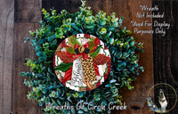 A wreath made of various green plants and a red ribbon with the word "Believe" written on it, placed on a wooden surface.