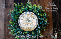 a wreath with a decorative plate containing a knight on horseback, surrounded by a lush green plant arrangement.