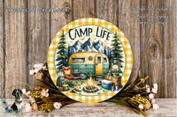 A round wooden plaque with a camping scene, including a camper van, campfire, and camping gear, surrounded by flowers and greenery.