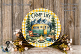 A round wooden plaque with a camping scene, including a camper van, campfire, and camping gear, surrounded by flowers and greenery.
