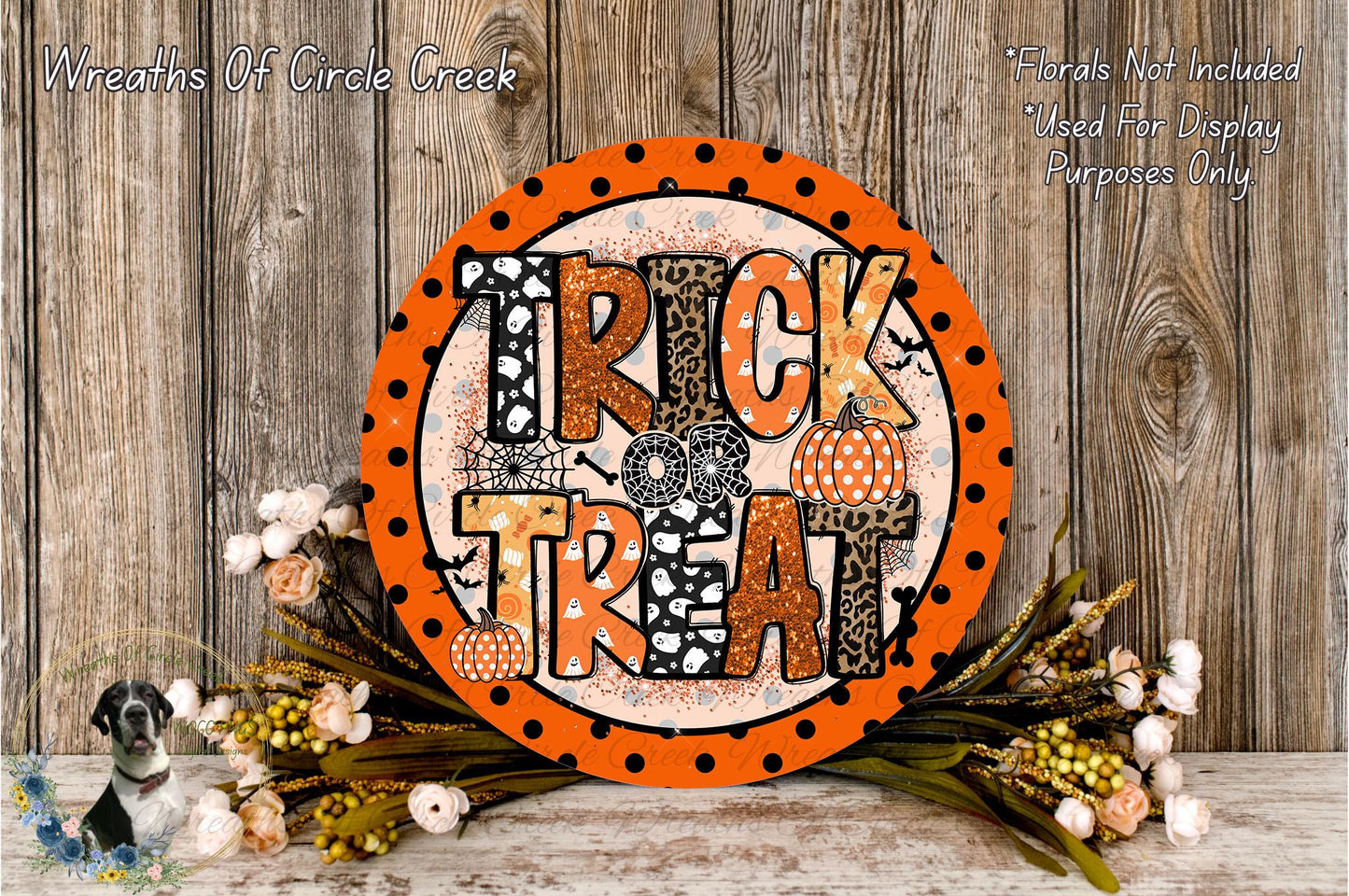 a Halloween-themed decoration with a large orange sign that says "TRICK TREAT" surrounded by a floral arrangement and a wooden background.