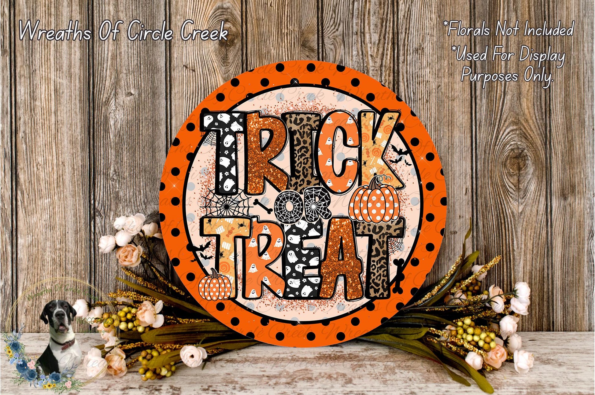 a Halloween-themed decoration with a large orange sign that says "TRICK TREAT" surrounded by a floral arrangement and a wooden background.
