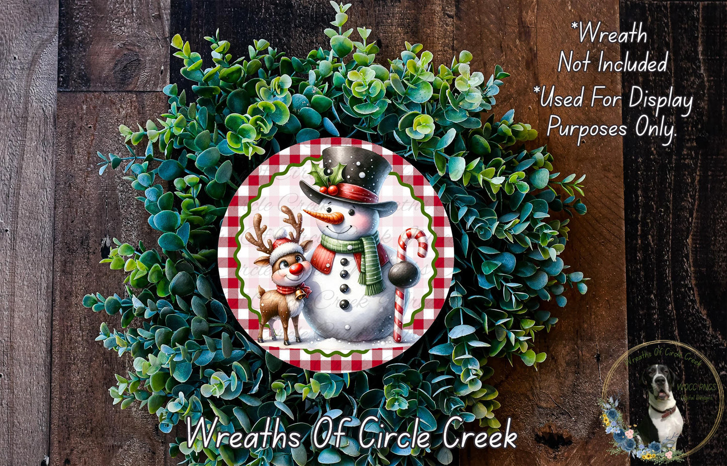 A wreath featuring a snowman and reindeer, surrounded by a lush green plant, with a wooden background.