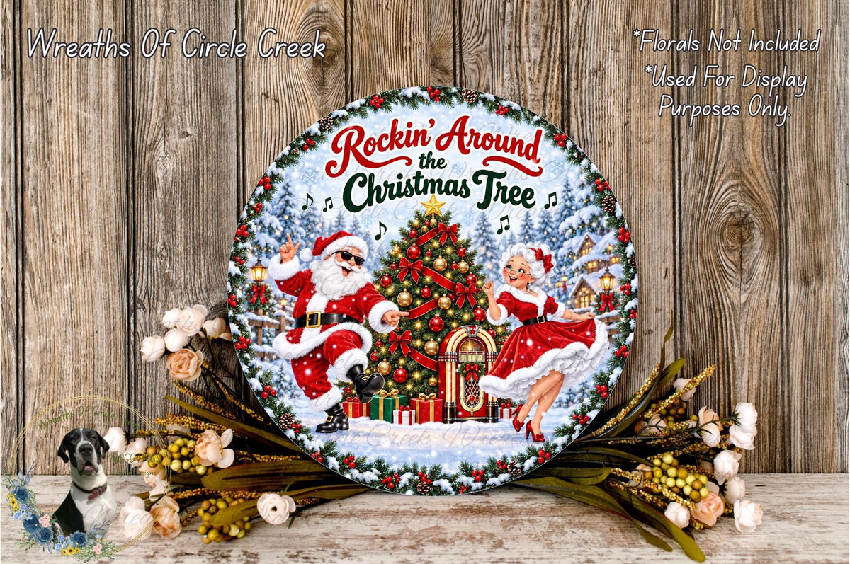 A decorative Christmas tree wreath with Santa Claus and a woman in a red dress, surrounded by flowers and greenery, placed on a wooden surface.
