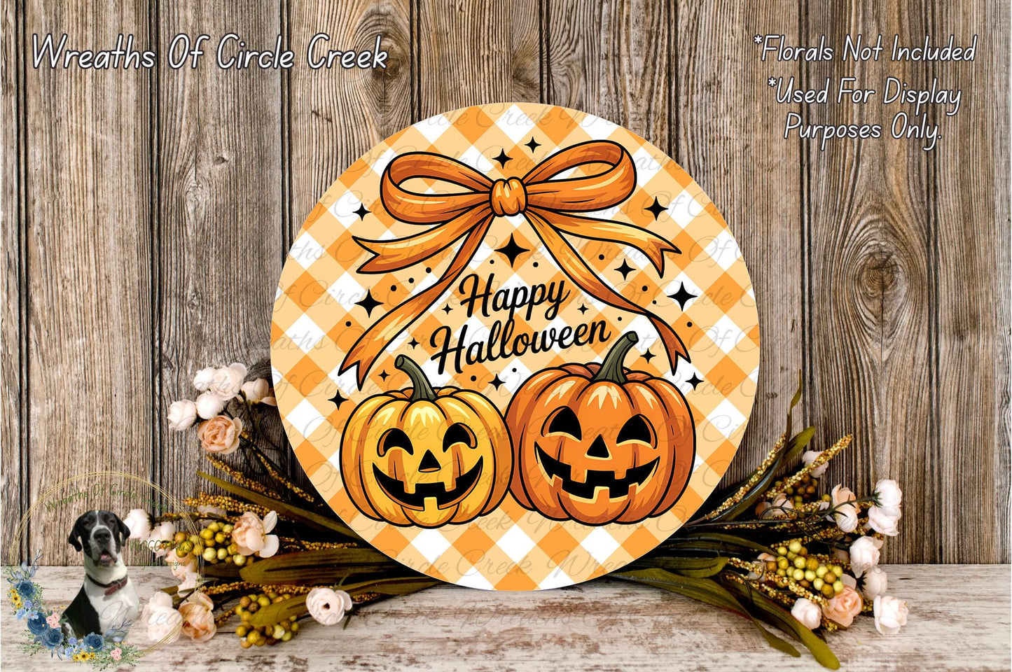 A Halloween-themed wreath with two jack-o'-lanterns and a bow, placed on a wooden surface with flowers and greenery.