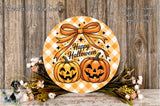 A Halloween-themed wreath with two jack-o'-lanterns and a bow, placed on a wooden surface with flowers and greenery.