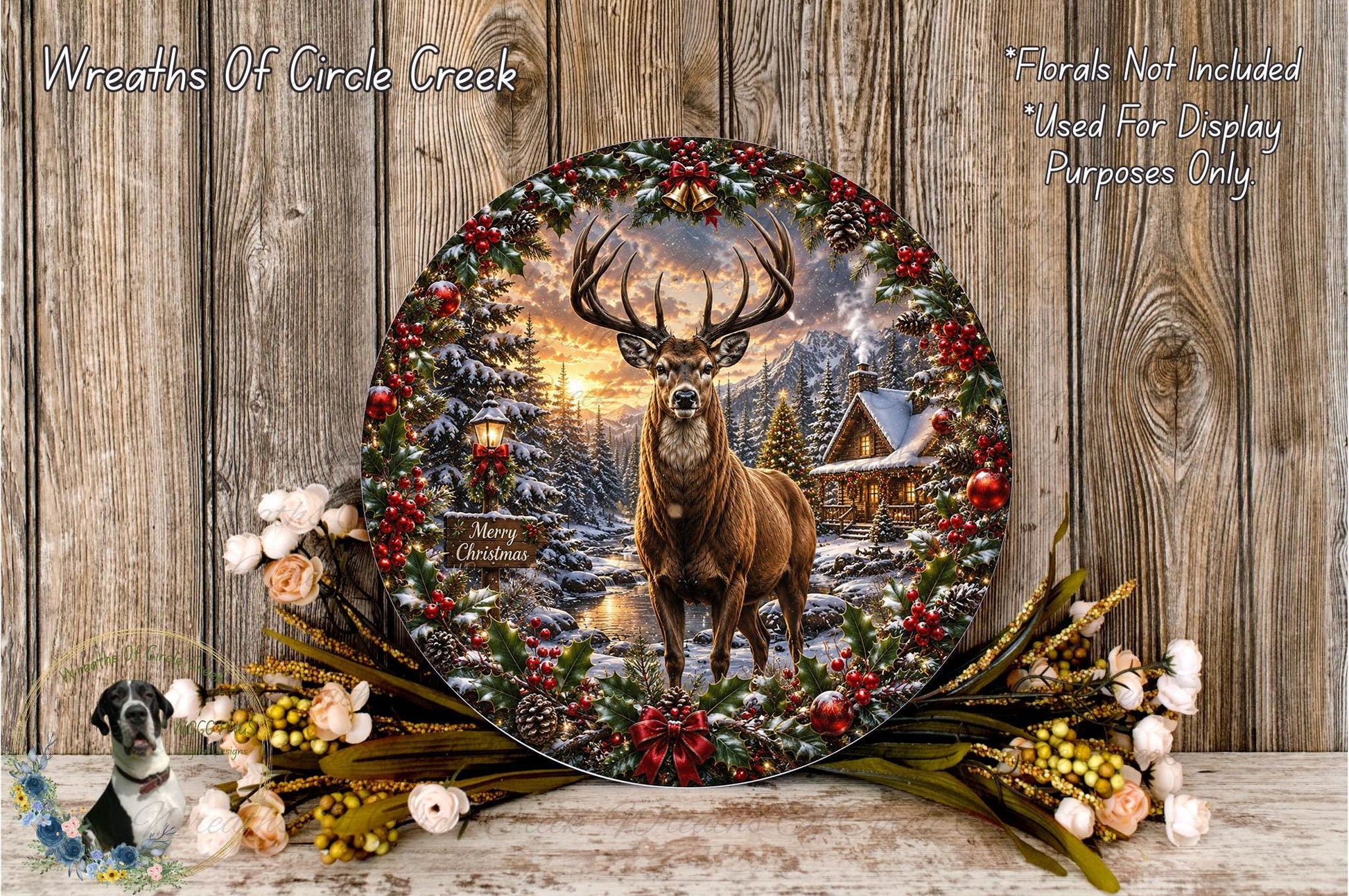 A decorative wreath featuring a deer surrounded by a snowy forest scene, with a cabin in the background. The wreath is placed on a wooden surface, and there are flowers and greenery surrounding it.