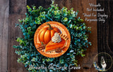 A wreath made of green foliage and a pumpkin with whipped cream on top, placed on a wooden surface.
