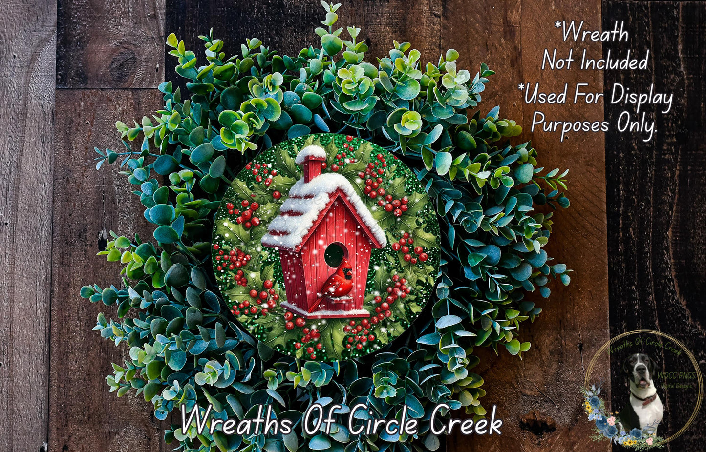 A wreath made of green leaves and red berries, with a small red birdhouse in the center, is displayed on a wooden surface.