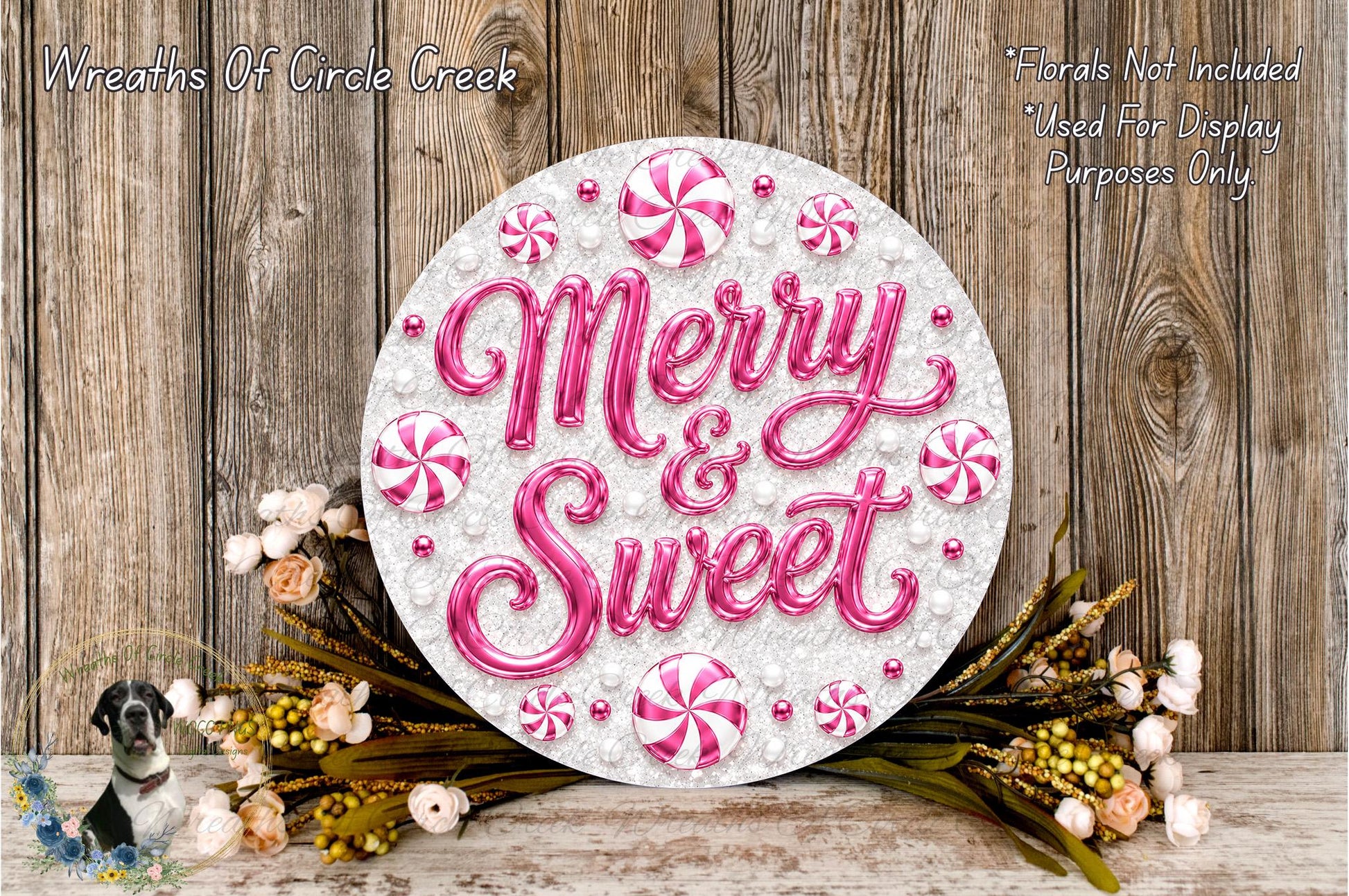 a decorative sign with the words "Merry & Sweet" written on it, surrounded by pink and white candy-like elements and flowers. The sign is placed on a wooden surface, and there are additional floral elements in the background.