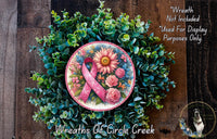 A wreath made of green leaves and flowers, with a pink ribbon and a large sunflower in the center. The wreath is displayed on a wooden surface.