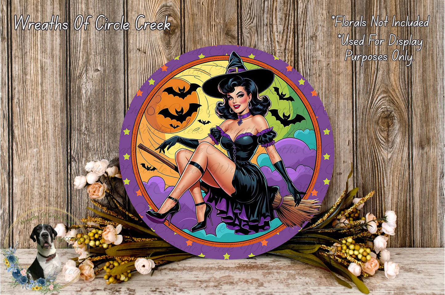 A round wall decoration featuring a woman dressed as a witch, with a Halloween-themed background and bats flying around. The decoration is surrounded by flowers and placed on a wooden surface.