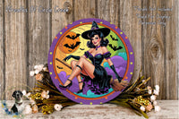 A round wall decoration featuring a woman dressed as a witch, with a Halloween-themed background and bats flying around. The decoration is surrounded by flowers and placed on a wooden surface.