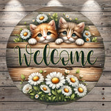 A wooden sign with two cute kittens peeking out from behind a floral arrangement, with the word "Welcome" written on it.