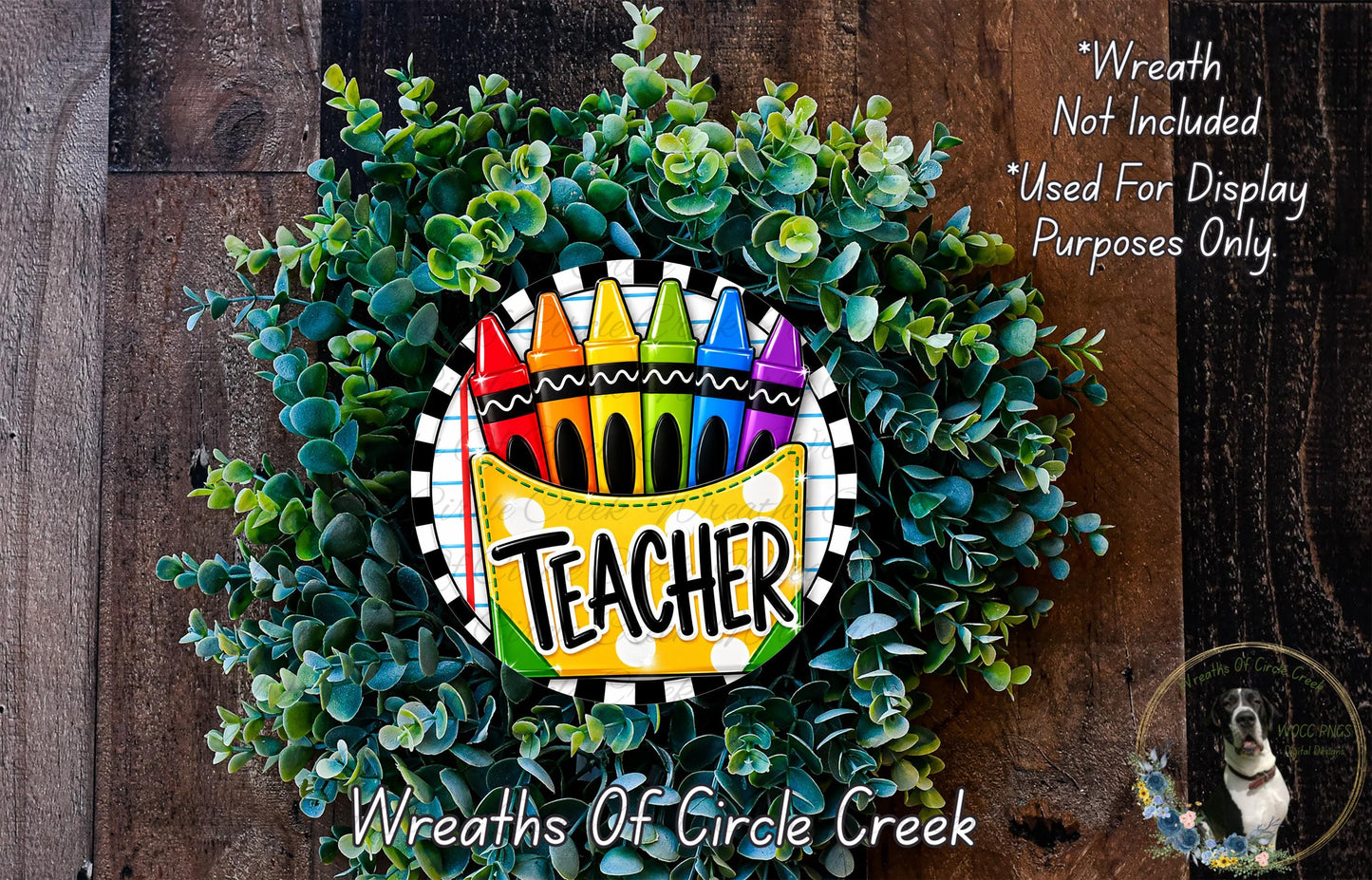 A wreath made of green leaves and crayons, with the word "Teacher" written on it, is displayed on a wooden surface.