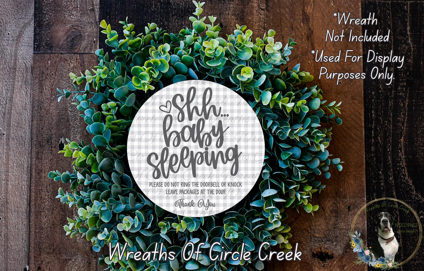 a wreath made of green leaves and a white circular sign with text on it, placed on a wooden surface.