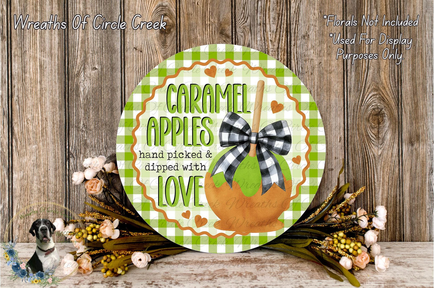 a round wooden sign with a checkered border and a decorative apple design, surrounded by a floral arrangement and a wooden background.