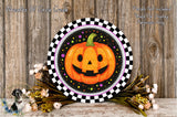 a Halloween-themed wreath with a jack-o-lantern design, placed on a wooden surface. The wreath is surrounded by a floral arrangement and has a checkered border.