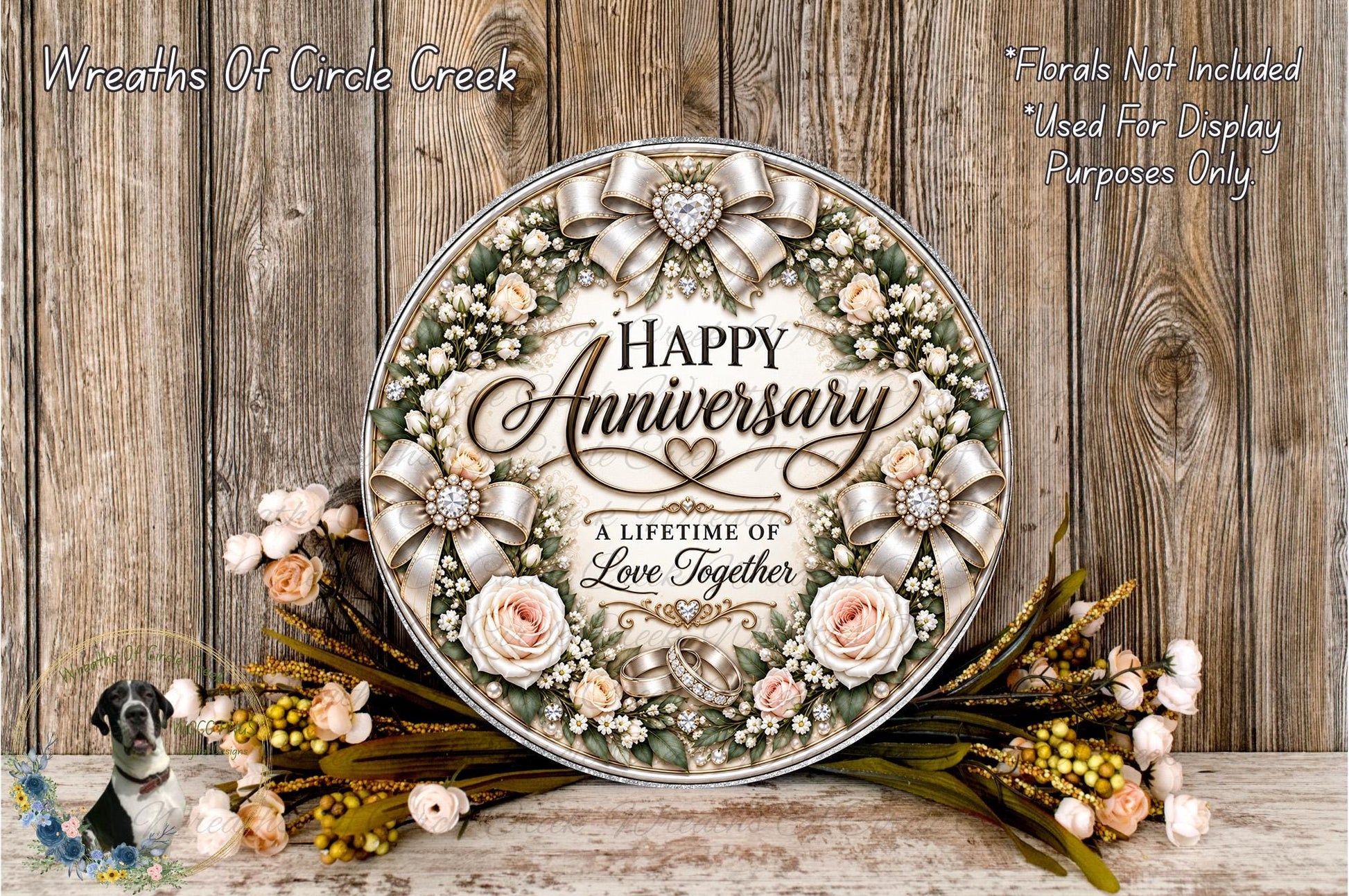 A decorative wreath with the text "Happy Anniversary" and "A Lifetime of Love Together" surrounded by flowers and greenery, placed on a wooden surface.