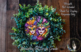 A wreath made of green leaves and flowers, featuring two colorful faces wearing masks, with a wooden background.