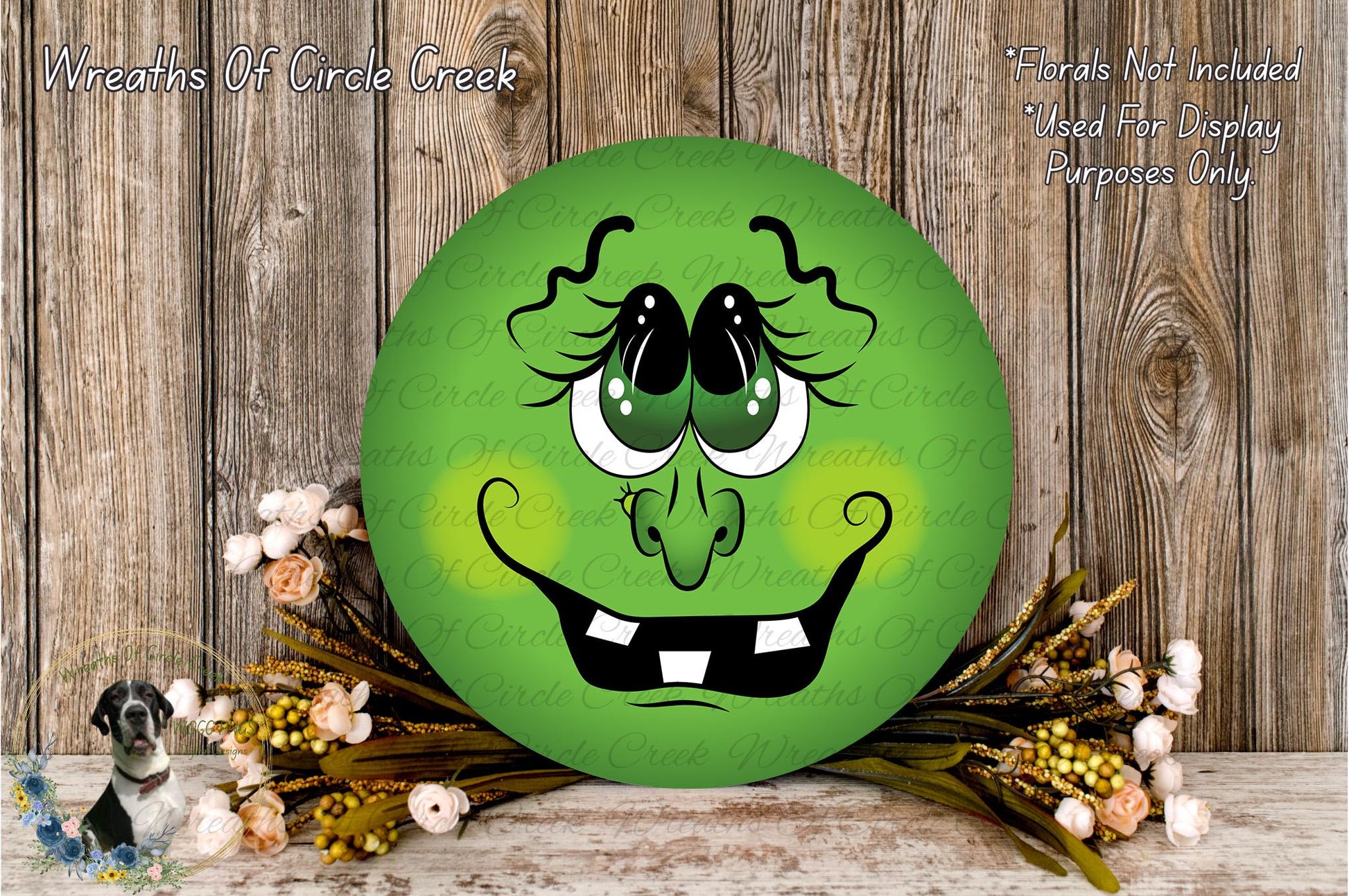 a green, round, cartoonish face with large eyes and a wide smile, surrounded by a wreath of flowers and a wooden background.