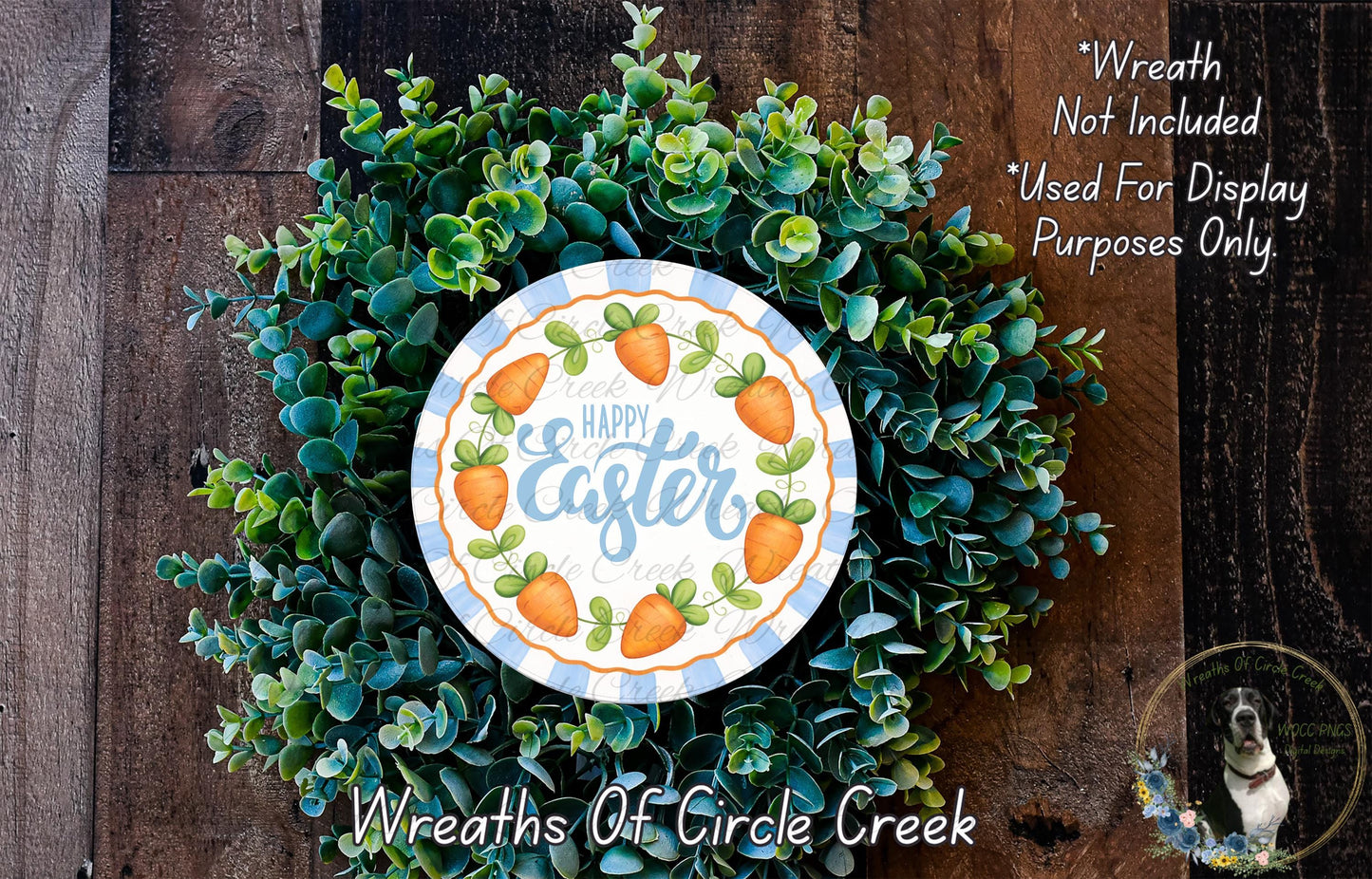 a wreath made of green foliage and orange carrots, with a decorative plate in the center that says "Happy Easter". The wreath is displayed on a wooden surface, and there is a small dog in the bottom right corner of the image.