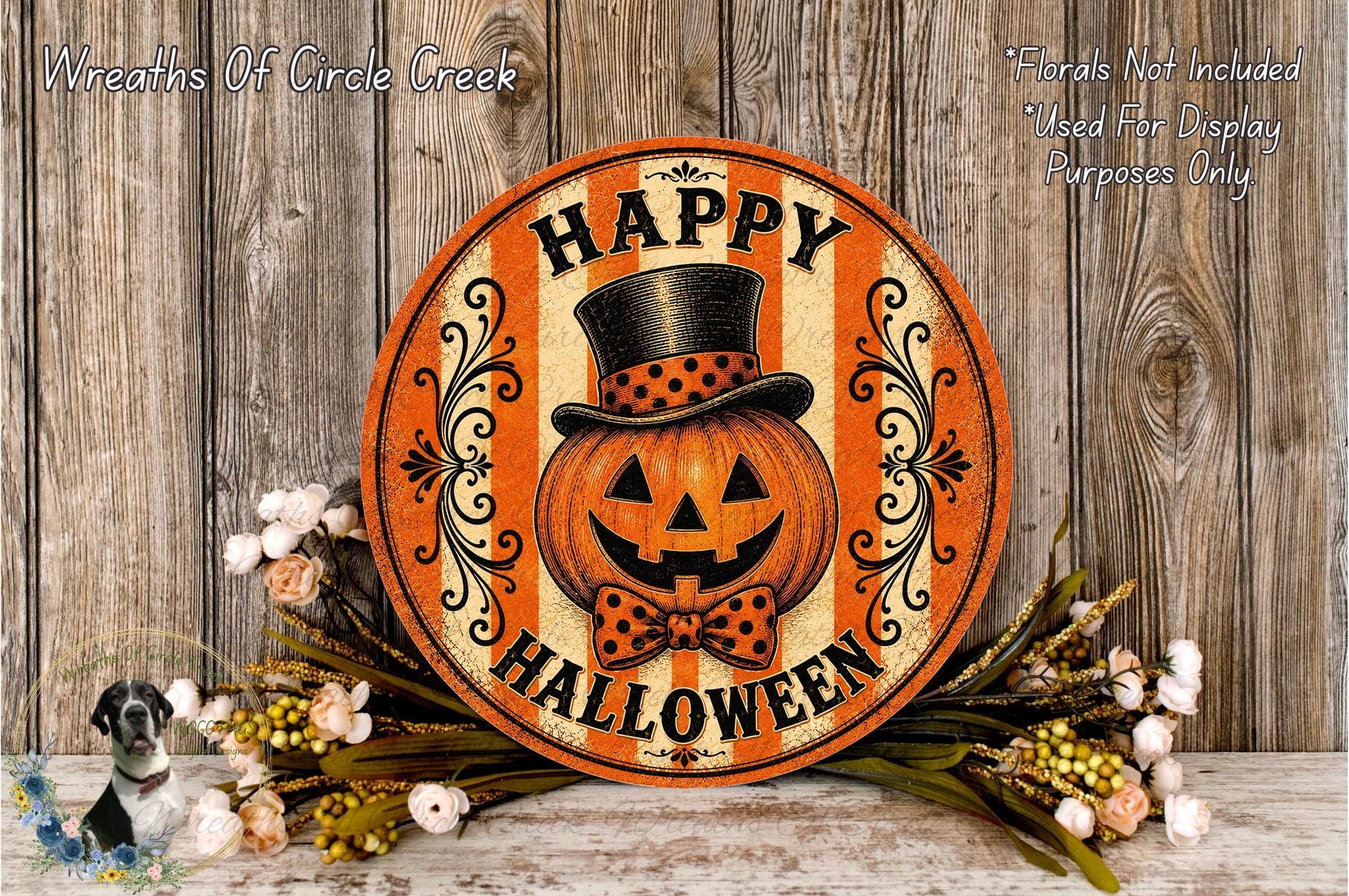A Halloween-themed sign with a jack-o-lantern and a bow tie, surrounded by flowers and placed on a wooden surface.