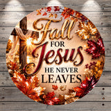 The image is a circular graphic with a wooden background and a cross, surrounded by autumn leaves in shades of red, orange, and gold. The text "Fall for Jesus he never leaves" is prominently displayed in the center of the image.